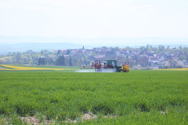 Das Bild zeigt ein landwirtschaftliches Gerät, mit vor dem Hintergrund eines deutschen Dorfes ein Feld bewirtschaftet wird. Foto: Johanna Fick